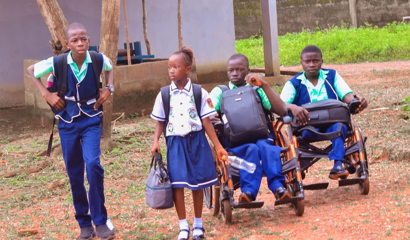 Three pupils in school uniform on their way to class, two of them using wheelchairs