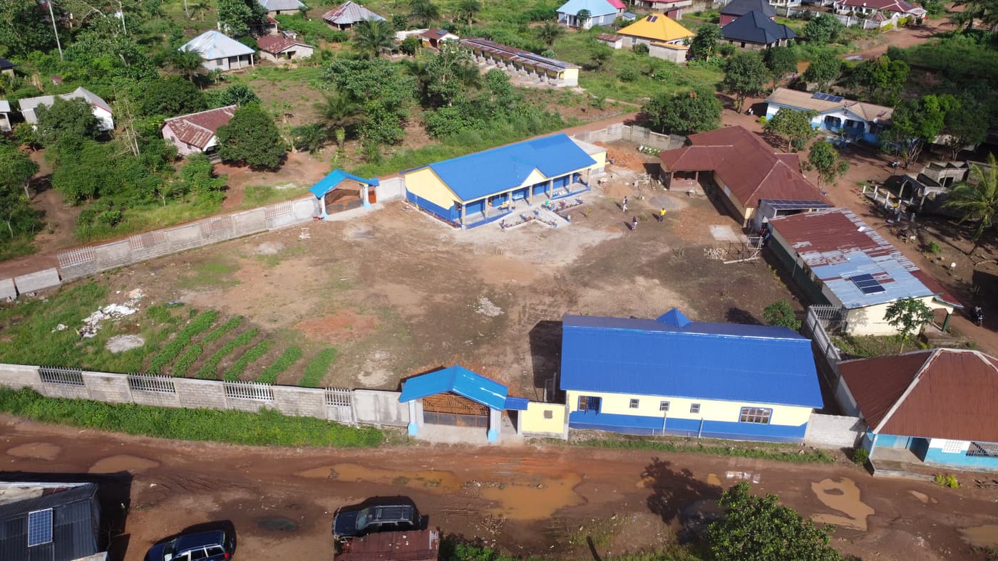 Aerial view of the Village of Hope in Kambia: blue-roofed school and training buildings inside a walled compound, with gardens along the wall
